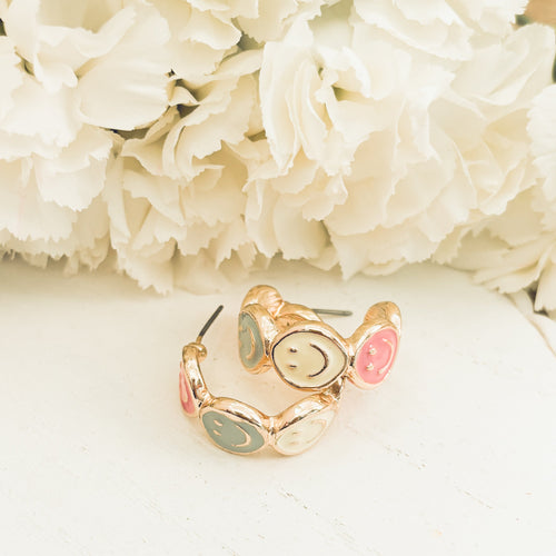 Pair of gold hoop earrings featuring smiling face charms, stylish and playful jewelry by Rooted Home Goods.